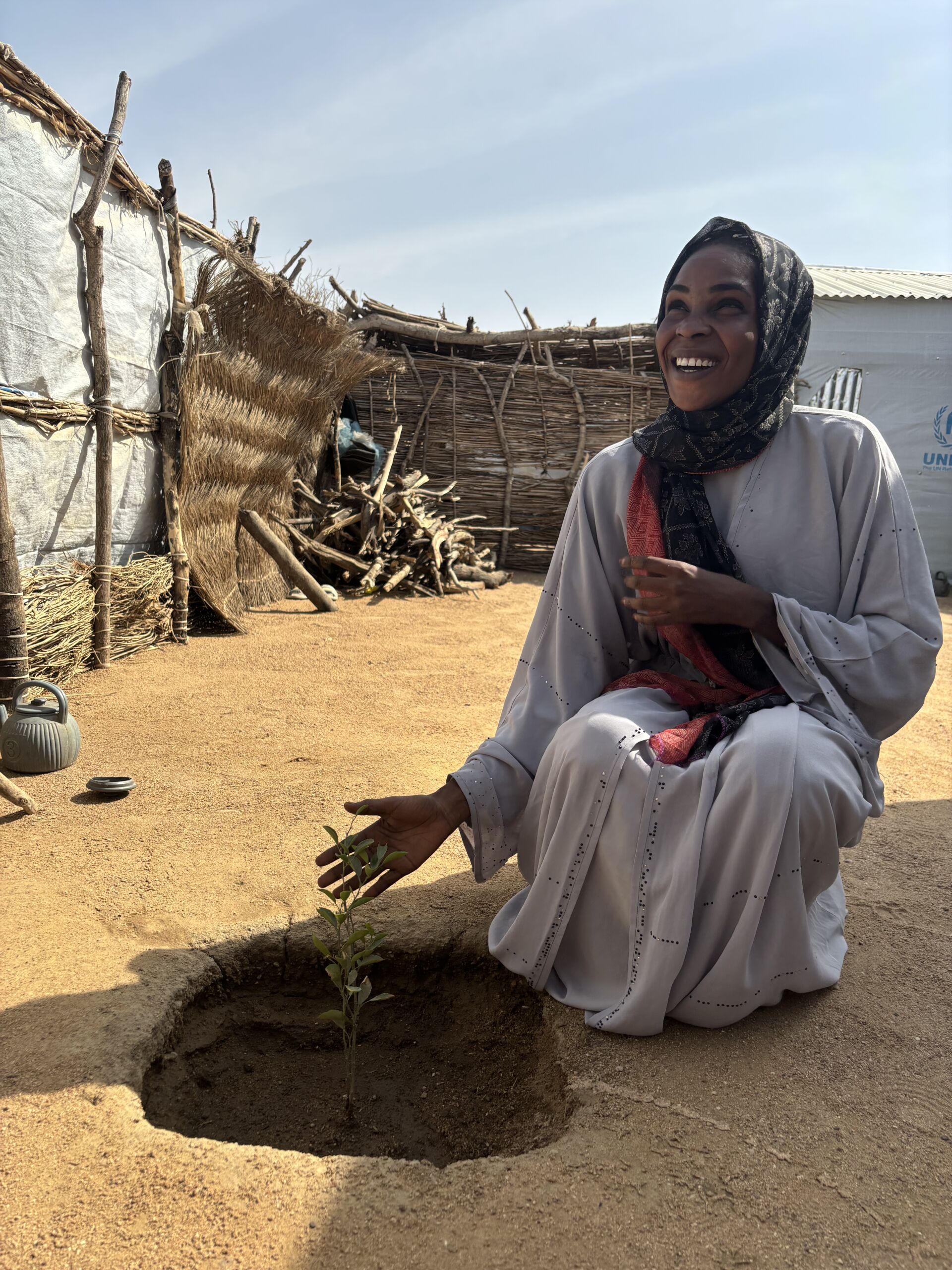 Sammen med Mission Easts partner, LM International, reagerer vi på det voksende behov for hjælp. Vores fokus er på Dougui-lejren, den sjette lejr langs grænsen til Sudan. På billedet ser vi en kvinde stolt fremvise det frugttræ, hun har plantet som en del af et projekt, der er blevet gennemført i samarbejde med Mission East og vores lokale partner.